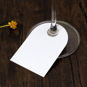 U-shaped white paper place card attached to a wine glass stem on a dark wooden table