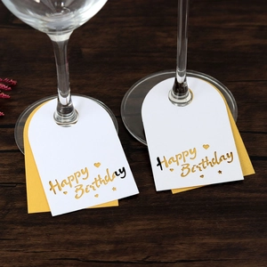 Detalle de tarjetas Happy Birthday blancas y doradas para copas sobre madera