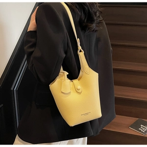 Detail of yellow bucket bag featuring lychee grain leather and brand logo on dark stairs