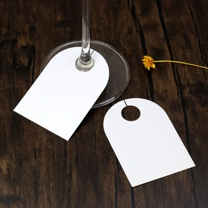 Detail of white arched wine glass name cards on dark wood table for wedding guest seating