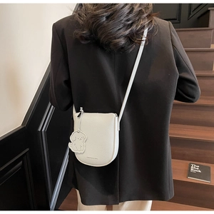 Détail du sac de selle en cuir blanc avec breloque chien sur un escalier noir
