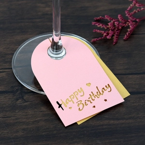Elegantes tarjetas de copa Happy Birthday en rosa y dorado sobre base de madera