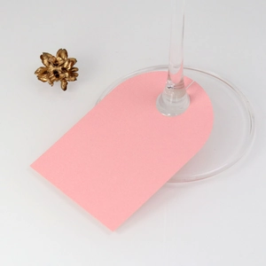 Close-up of a pink arched paper wine glass card with a cutout on a clear glass stem