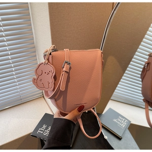 Détail du sac selle rose pêche avec texture litchi et breloque chien sous une lumière douce