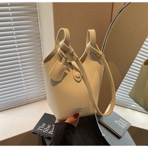 Detail of beige bucket bag in lychee texture leather with branded logo and hand strap