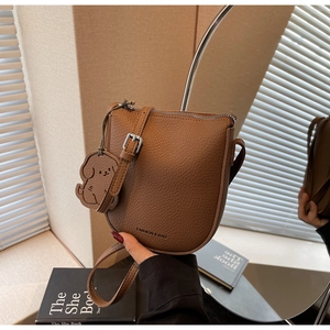 Détails d'un sac selle en cuir marron avec charme de chien et fermeture éclair en métal