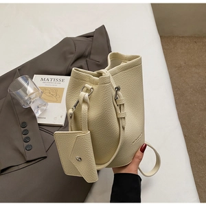 Detailed close-up of cream-white bucket bag with lychee grain texture and a mini pouch
