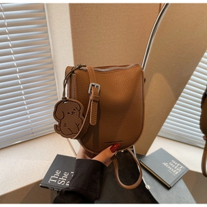 Détail du sac de selle en cuir grainé marron avec lettrage et charm de chien