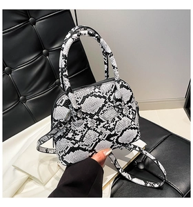 Detail shot of chic snakeskin shell bag featuring dual top handles and metal zipper hardware