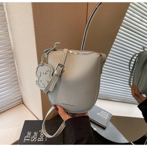 Détail d'un sac selle en cuir grainé gris clair avec breloque chien et boucles argentées