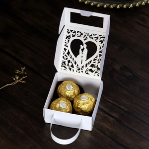 Macro view of white laser-cut wedding candy box with heart pattern and ribbon handle