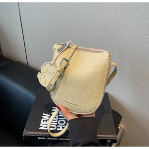 Détail d'un sac selle jaune clair avec texture litchi et accessoire de charme de chien