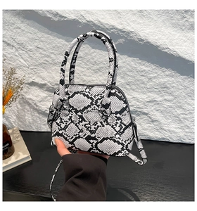 Detailed shot of snakeskin texture on a shell-shaped crossbody bag with dual handles