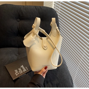 Close-up of cream pebble grain leather bucket bag featuring a sleek wide handle and logo