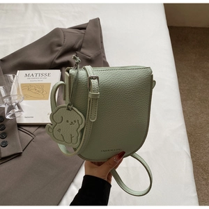 Détail du sac selle en cuir vert menthe avec pendentif chien et texte embossé
