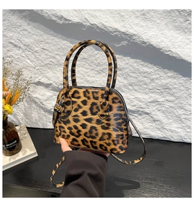 Detail of glossy leopard print shell bag with dual handles and golden hardware
