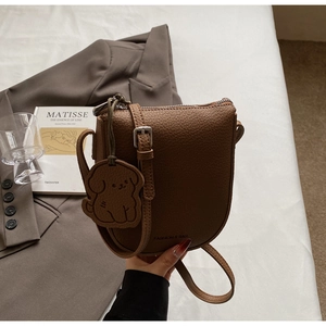 Détail d'un sac selle en cuir marron avec motif litchi et un charmant pendentif chien en cuir