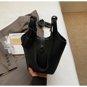 Detail of black pebbled leather bucket bag with top handles and adjustable strap