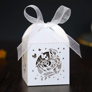 Macro detail of white laser-cut wedding favor box with rose patterns and ribbon