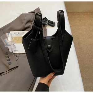 Detail of black lychee grain leather bucket bag with top handles and circular buckle