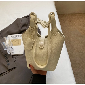 Close-up of off-white lychee grain leather bucket bag held by hand in elegant setting