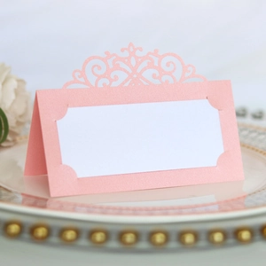 Close-up of pink laser-cut place card with ornate crown pattern on an elegant plate
