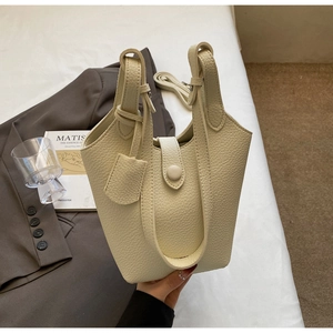 Close-up of cream pebble-grain bucket bag with detachable strap and leather charm tag