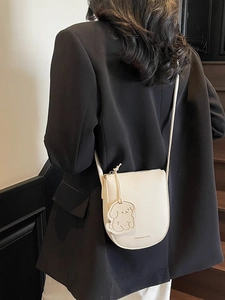 Sacoche chic en cuir beige avec breloque chien sur une mannequin en tailleur noir chic