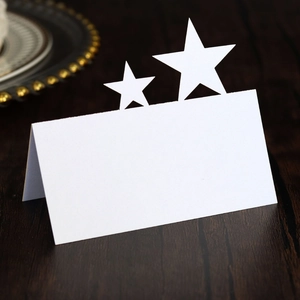 Close-up of a white fold-out table name card with hollow pentagram star cutouts on wood
