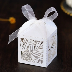 Detail of laser-cut tropical leaf patterns and white ribbon bow on wedding favor box