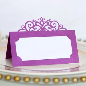 Detailed laser-cut purple glitter place card with ornate baroque pattern on a ceramic plate