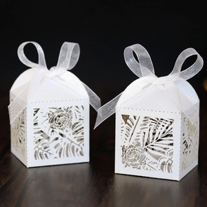 Detail of white laser-cut wedding favor box with tropical leaf patterns and ribbon