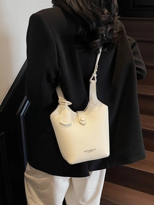 Minimalist beige bucket bag with pebble texture leather shown on a model in a black suit
