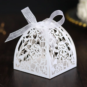 Macro shot of white laser-cut floral wedding candy box with delicate organza ribbon bow