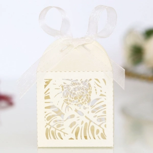 Detail view of laser-cut tropical leaf patterns on ivory wedding favor candy box with bow