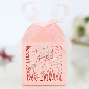 Close-up of pink laser-cut favor box with tropical leaf patterns and silk ribbon bow