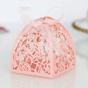 Detail of pink laser-cut wedding favor box with floral patterns and organza ribbon bow