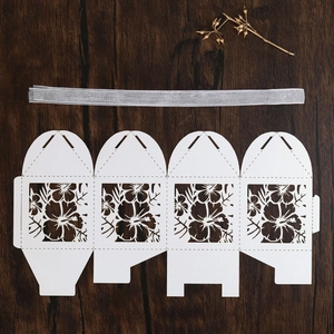Flat lay of laser-cut white candy box with hibiscus hollow design and silver ribbon