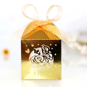Macro shot of laser-cut gold wedding candy box with rose pattern and silk ribbon bow