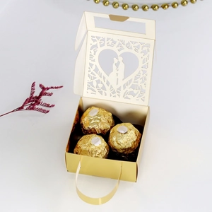 Detail of laser-cut gold wedding candy box with heart pattern and ribbon handle