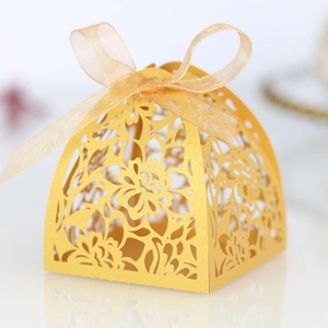 Detail of laser-cut gold wedding candy box with elegant floral hollow patterns and ribbon