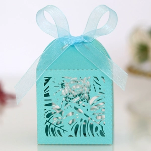 Detail of laser-cut tropical leaf patterns on sky blue gift box with organza ribbon bow