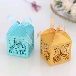Detail of laser-cut wedding favor boxes with monstera leaf patterns and satin ribbons