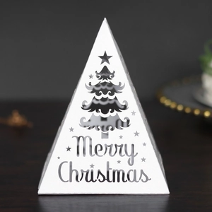 Macro shot of laser-cut Merry Christmas patterns on white pyramid gift box with LED lights