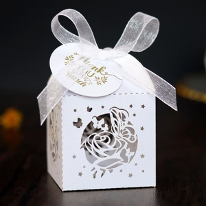 Macro detail of laser-cut white favor box with elegant rose butterfly patterns and ribbon