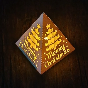 Pyramid Christmas lantern with star and tree cutouts glowing in warm yellow light