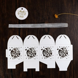 Flat lay of laser-cut white candy box with rose patterns, silver ribbon, and thank you card