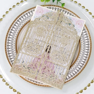 Detail of laser-cut glitter gold wedding invitation with floral insert on a plate