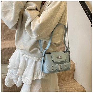 Détail du sac seau bleu clair avec fermoir rotatif argenté et sangle décorative à boucles