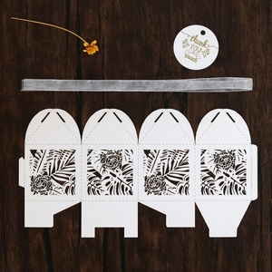Flat lay of laser-cut white gift box template with tropical leaf patterns and grey ribbon